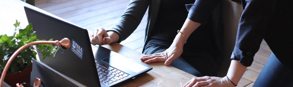 Two people lean on a desk to look at a laptop