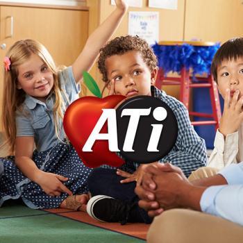 Three children sitting on a mat on the floor, one has their hand raised for a question